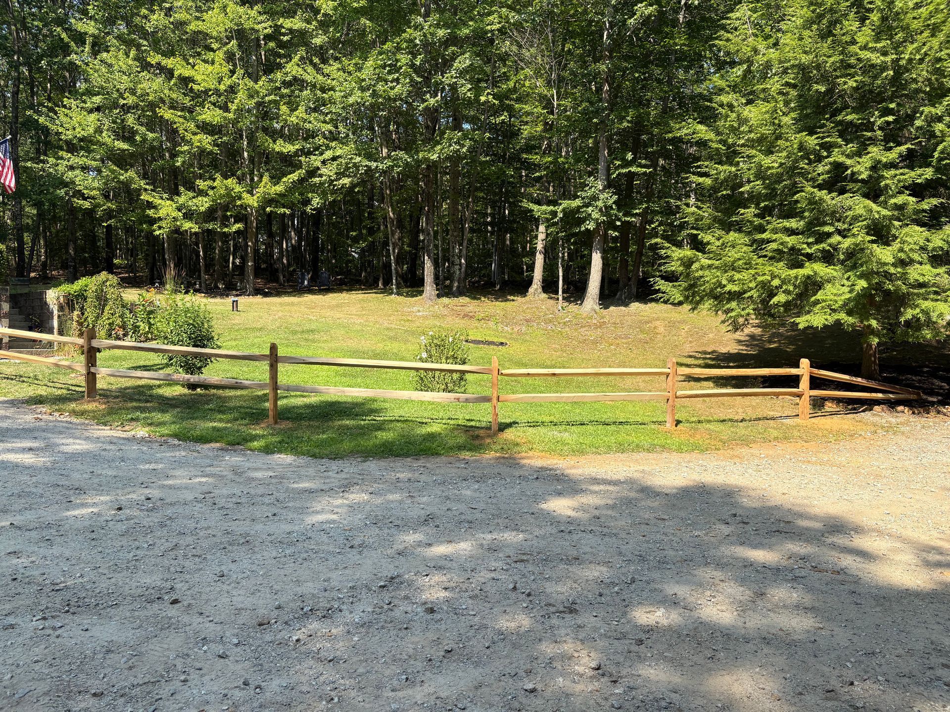 A wooden fence surrounds a grassy field in the middle of a forest.