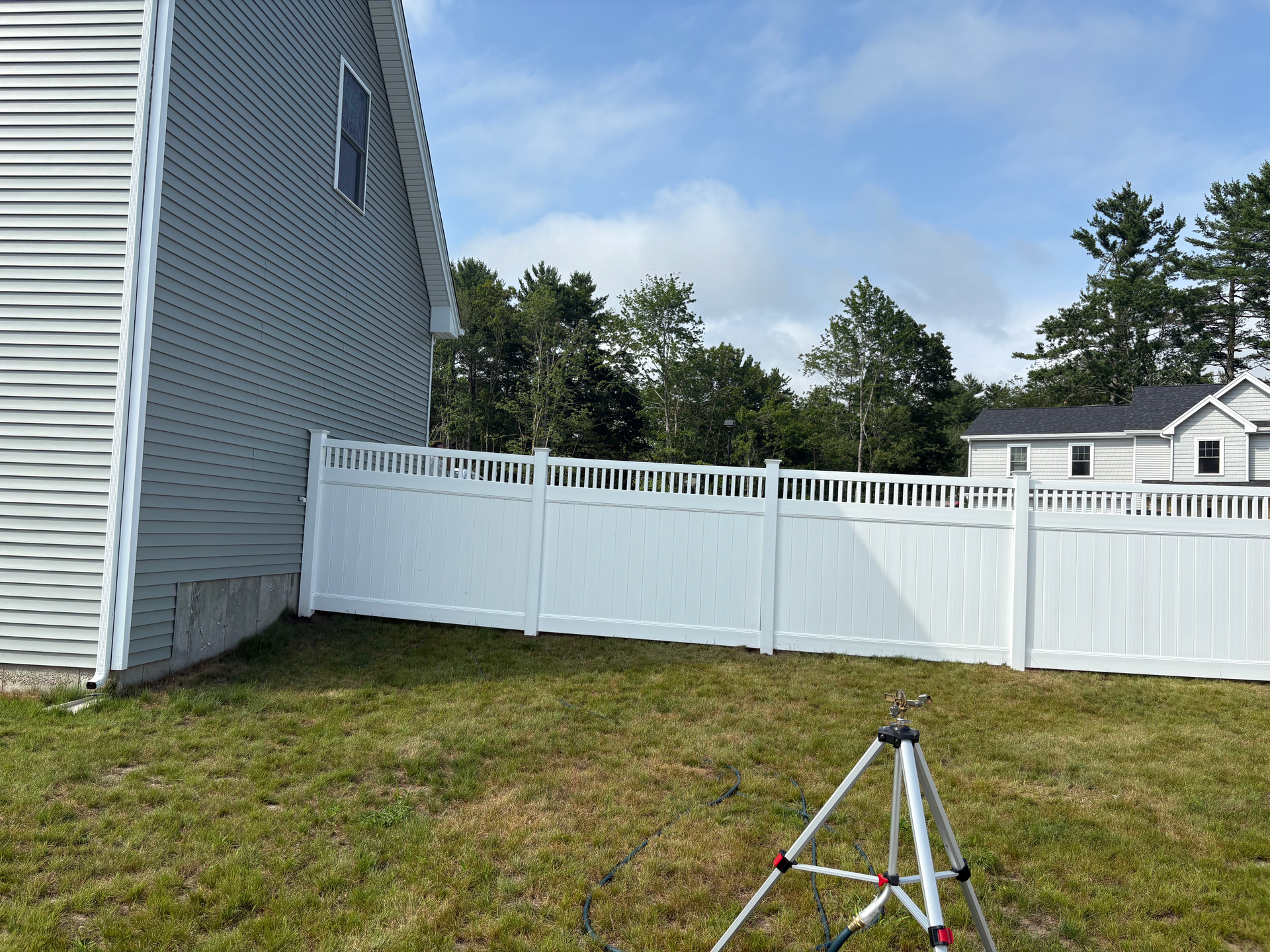 A white fence is in the backyard of a house.