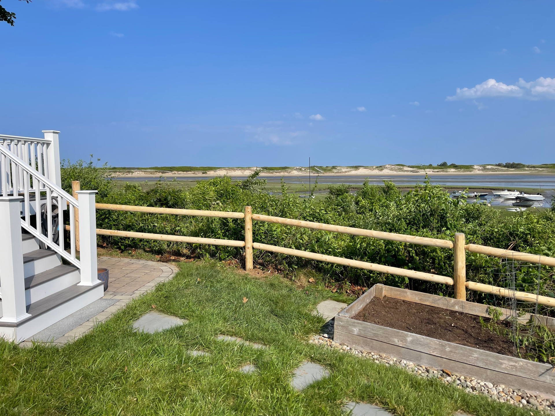 A wooden fence surrounds a yard with a view of a body of water.