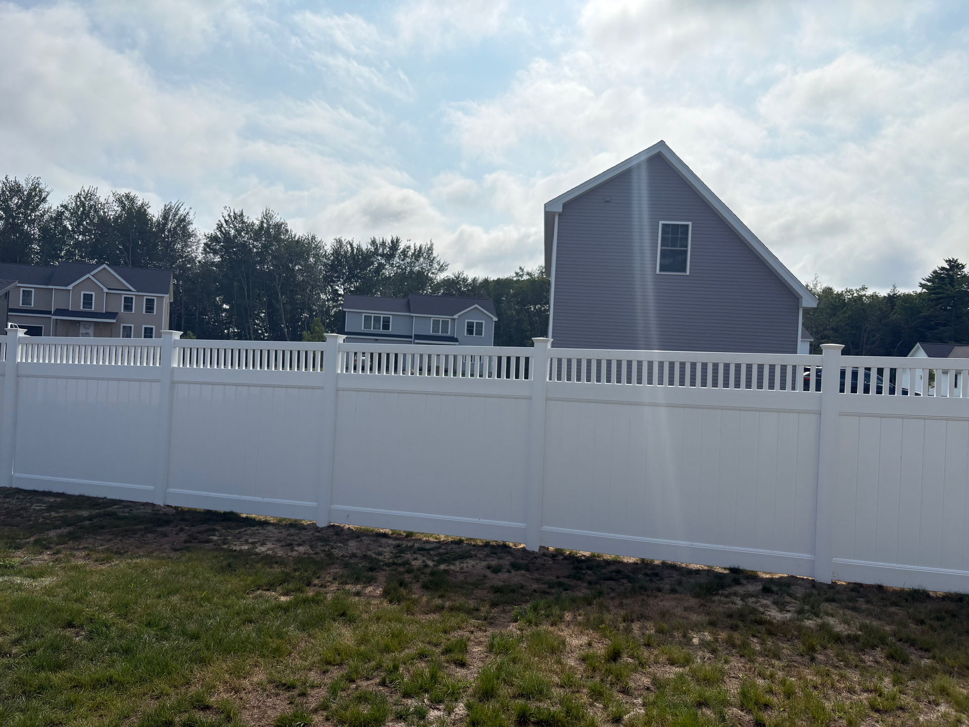 A white fence surrounds a grassy field in front of a house.
