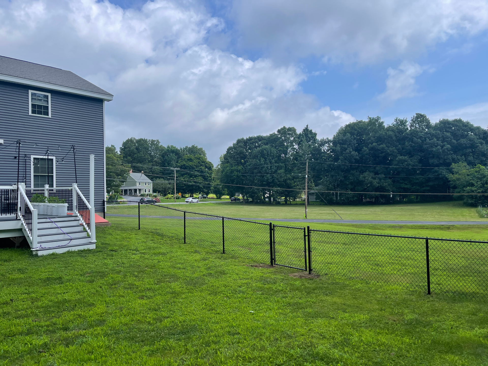 A house is sitting in the middle of a lush green field next to a chain link fence.