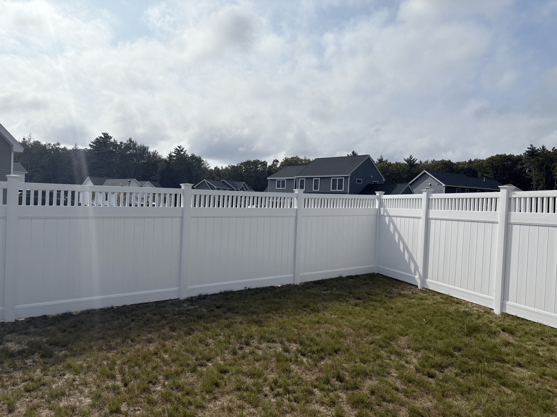 A white fence surrounds a lush green yard with a house in the background.