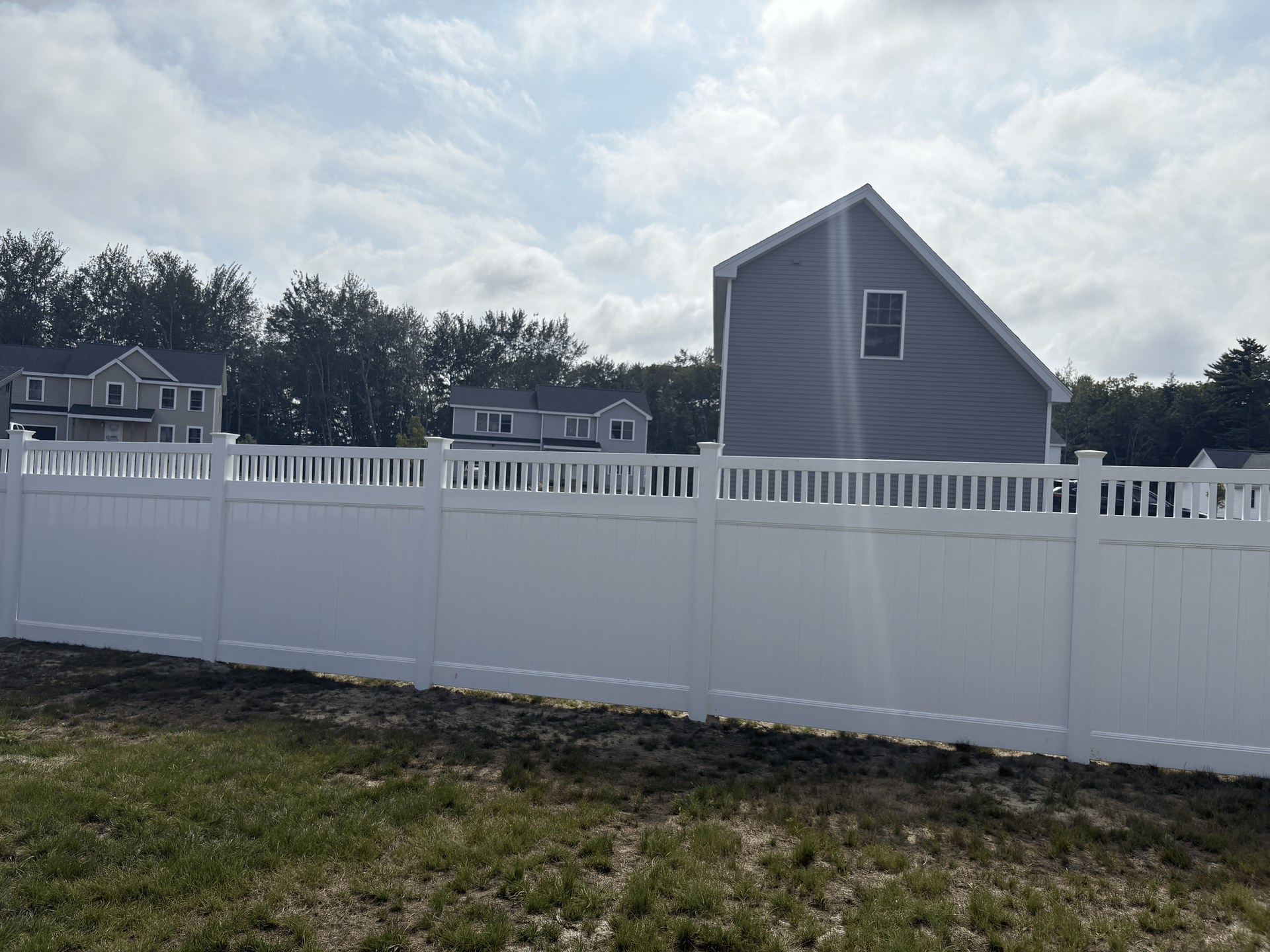 A white fence surrounds a grassy field in front of a house.