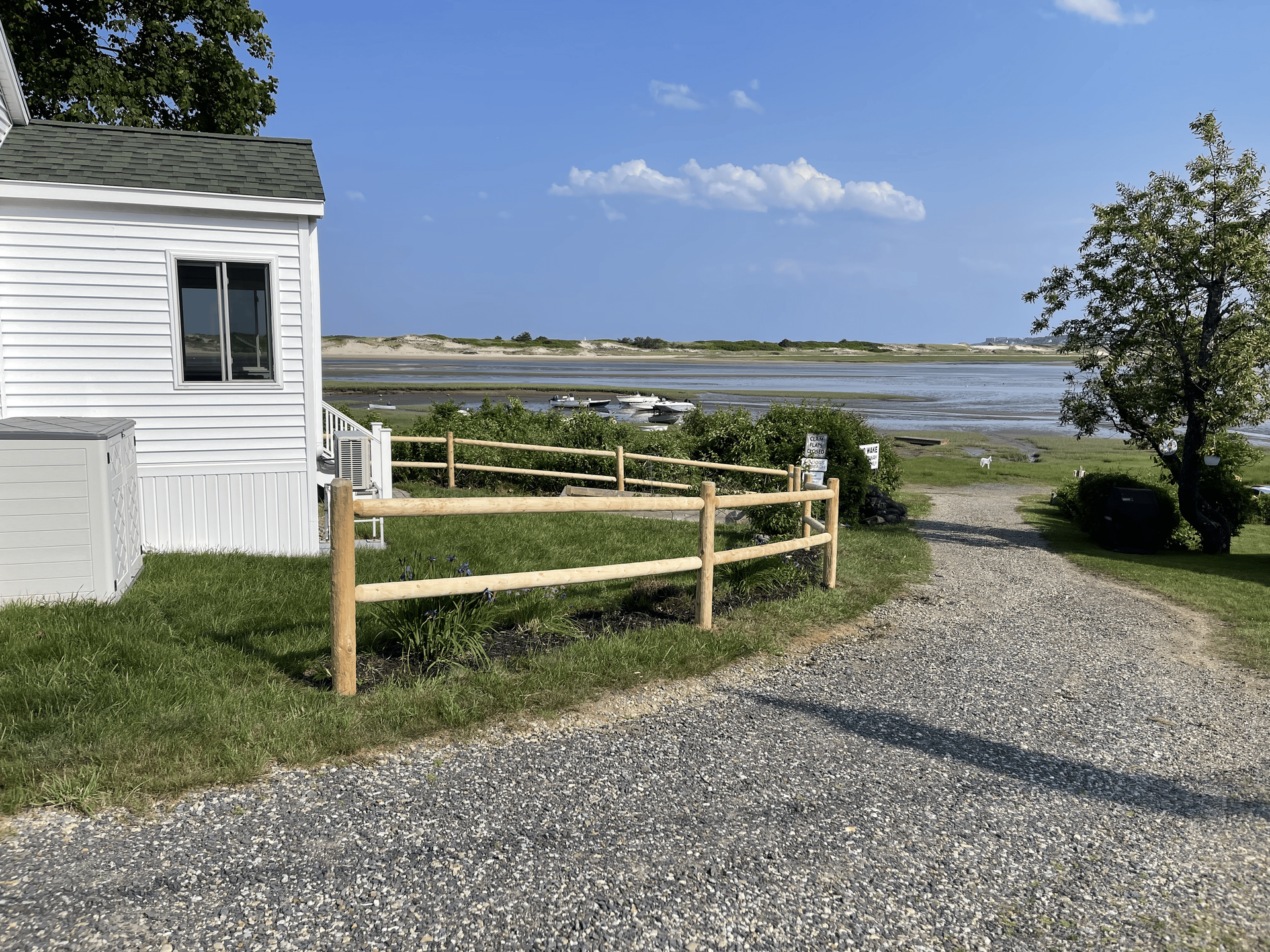 A white house with a wooden fence and a gravel driveway leading to it.