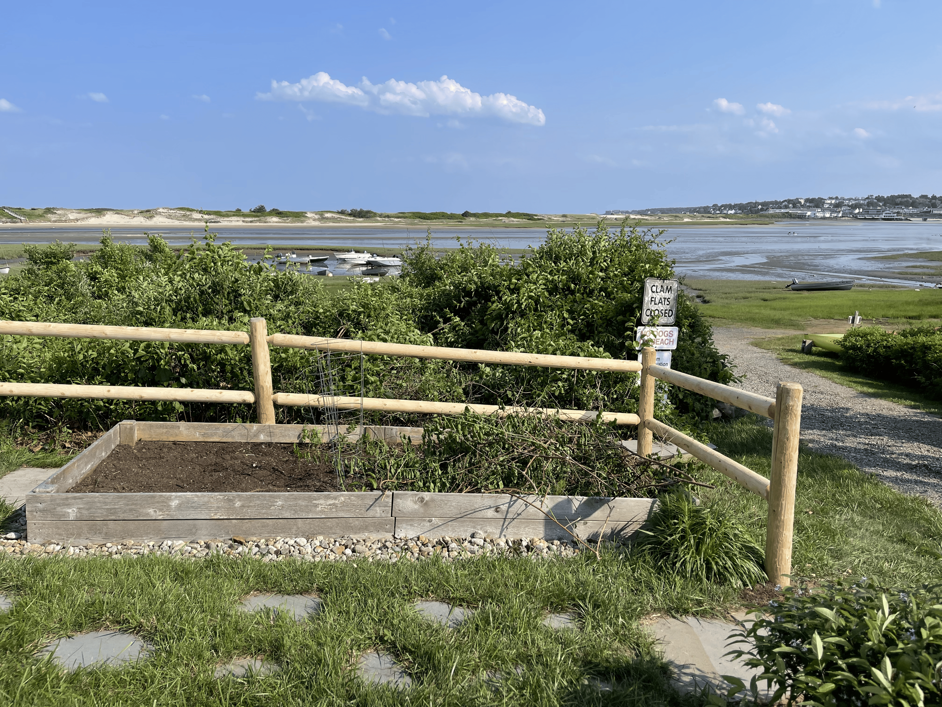 A wooden fence surrounds a garden with a view of a body of water.