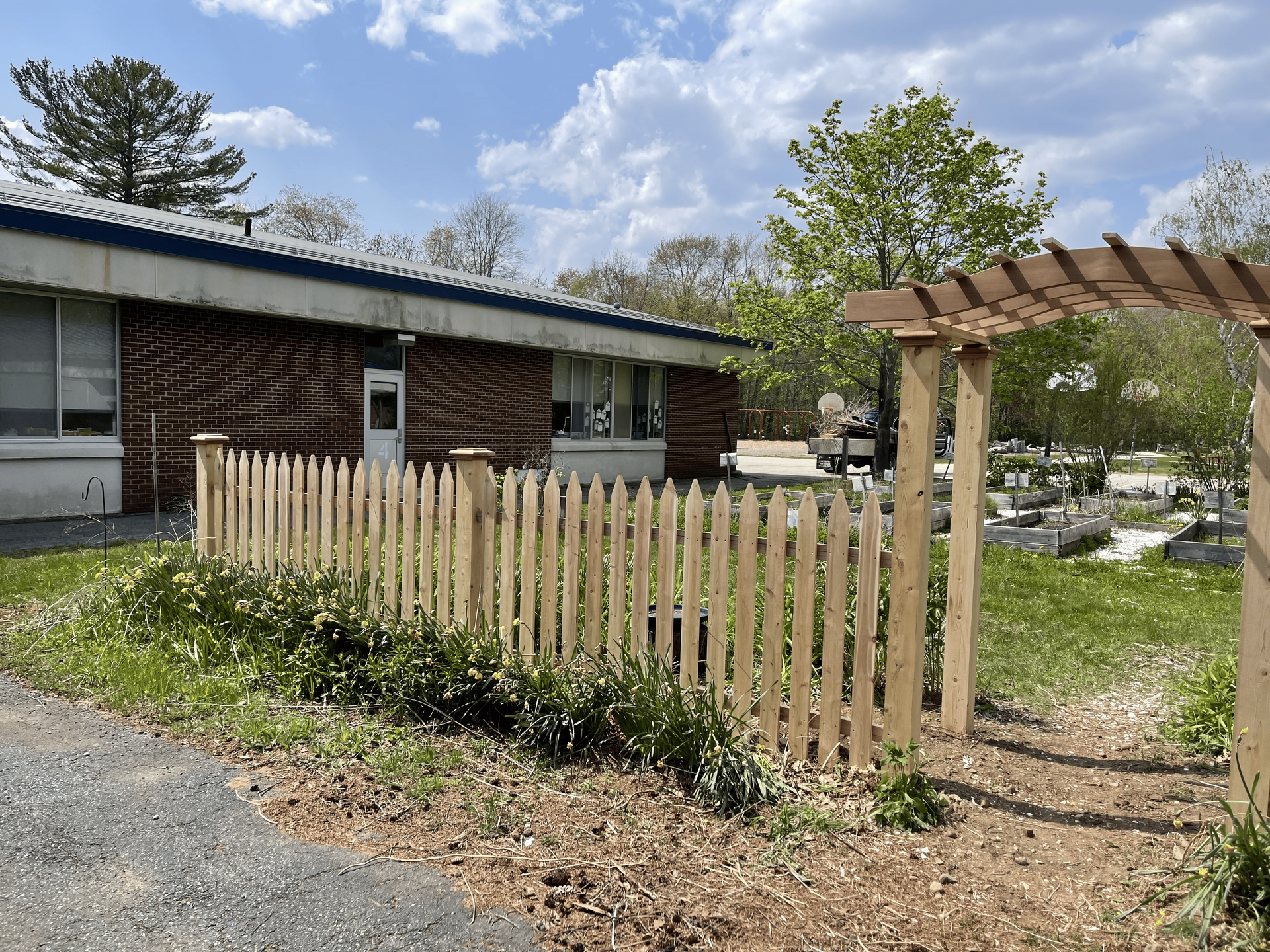A wooden picket fence is in front of a brick building.