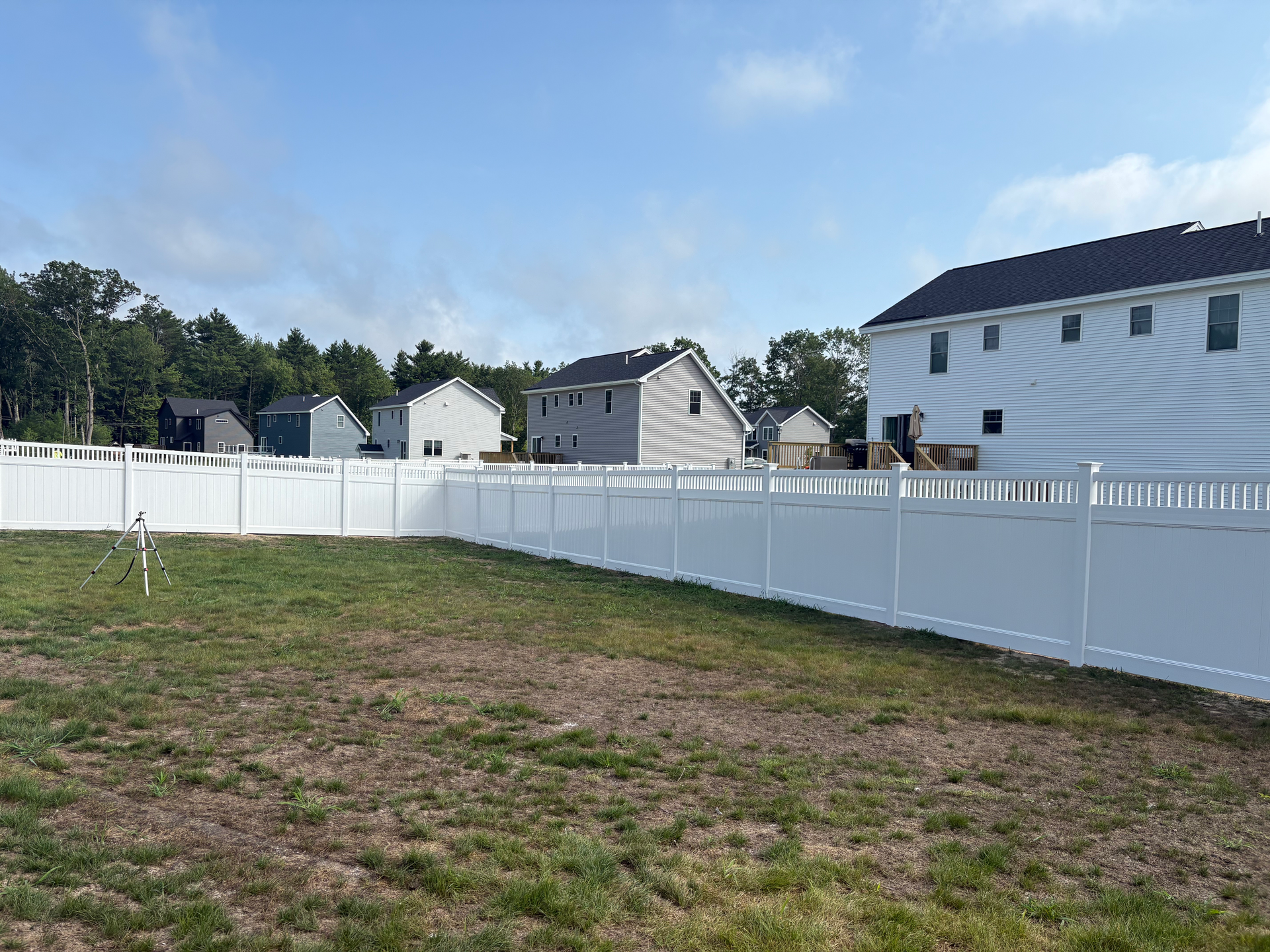 A white fence surrounds a grassy field in front of a house.