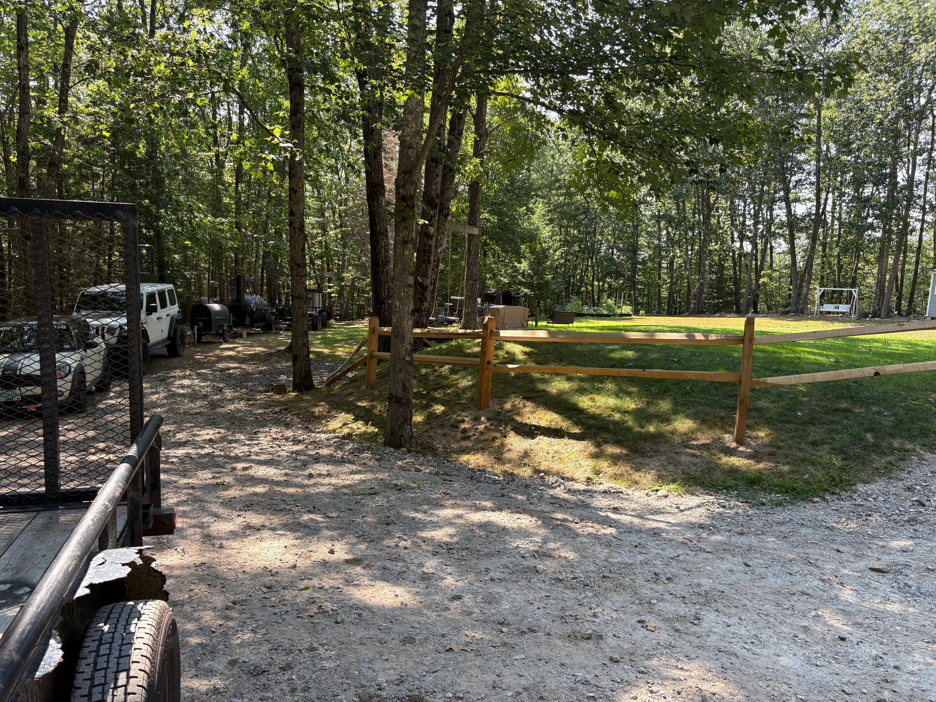 A trailer is parked in a gravel driveway next to a wooden fence.