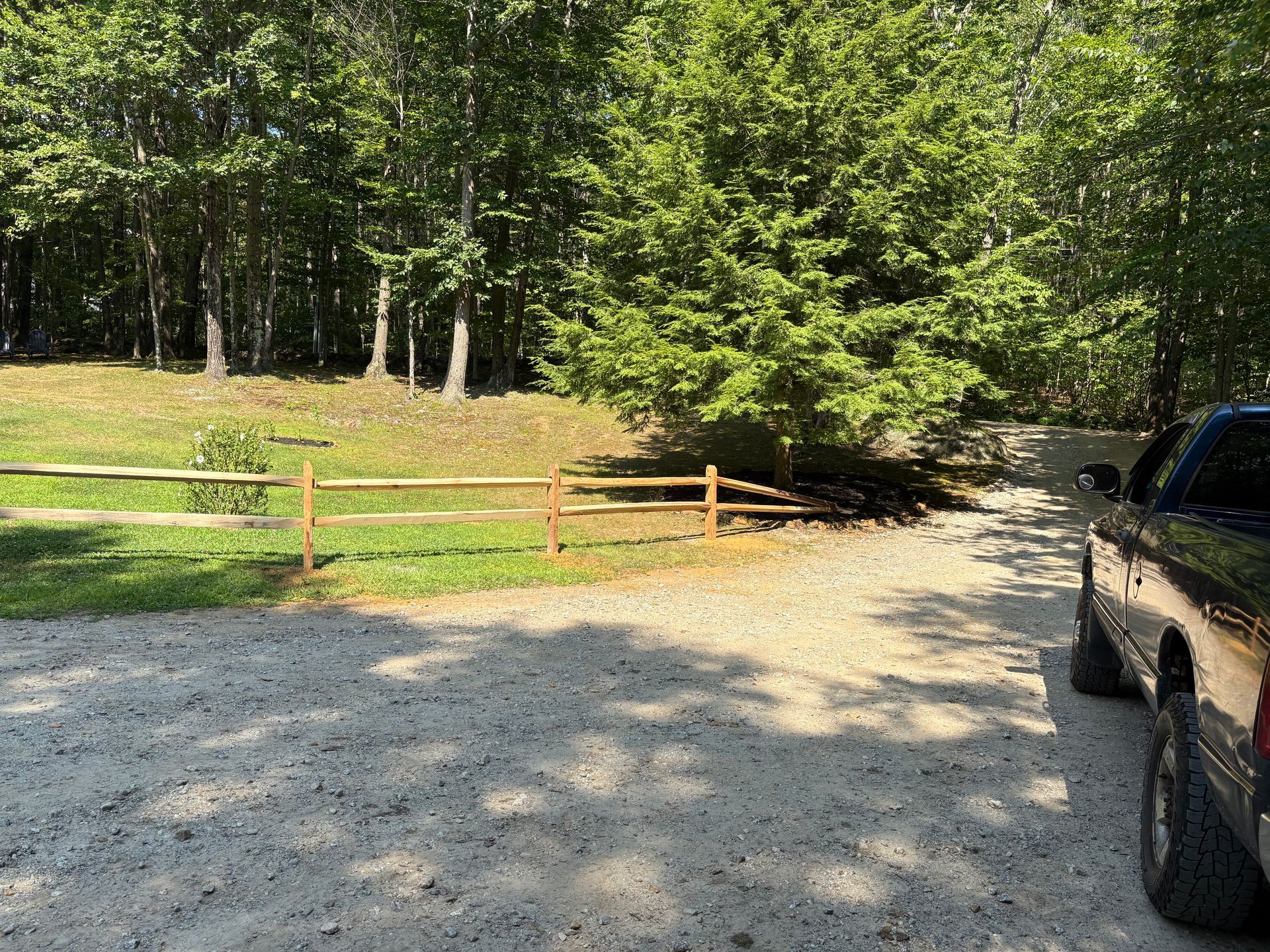 A truck is parked in a gravel driveway next to a wooden fence.