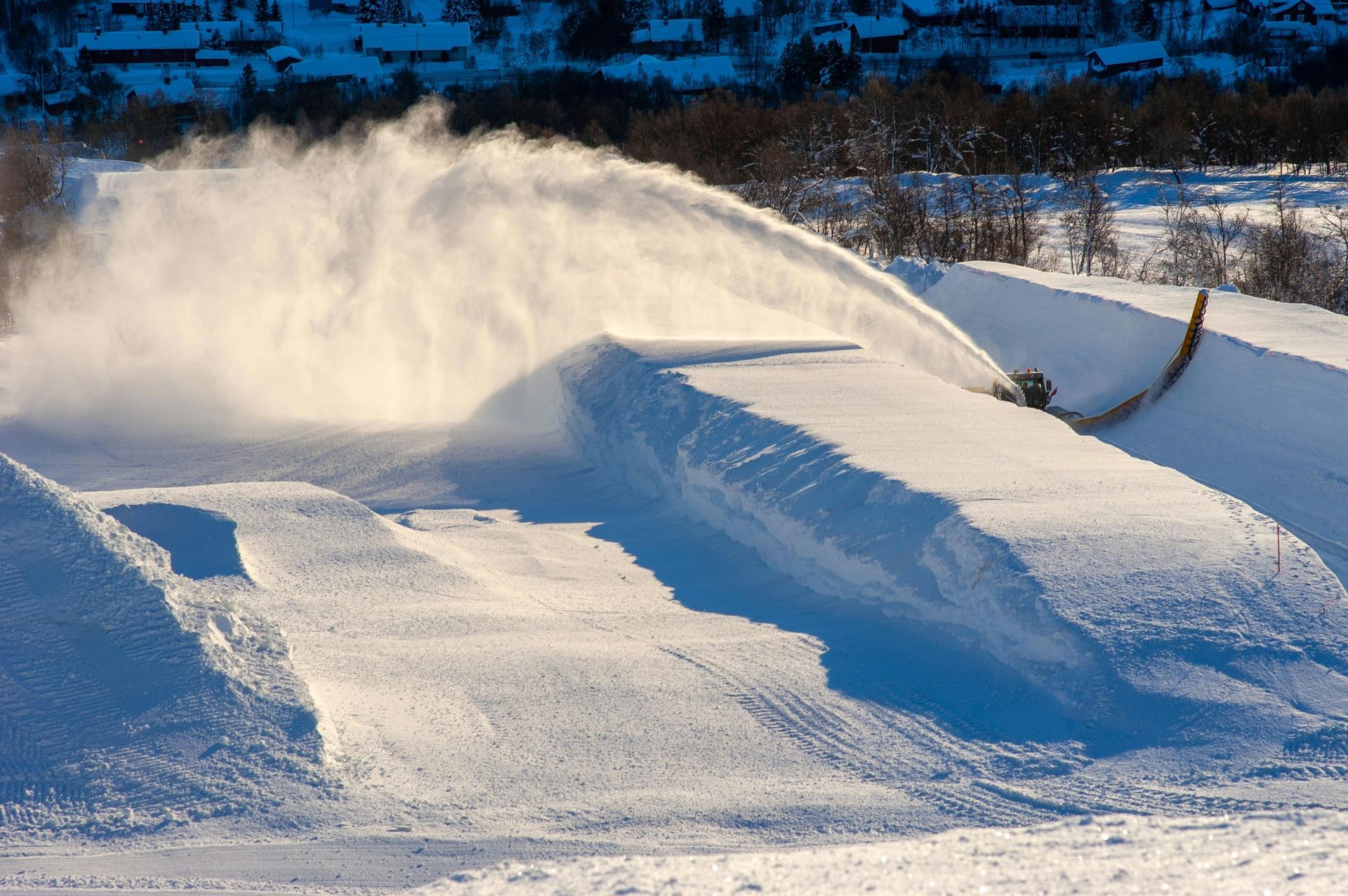 A snow blower is blowing snow on a snowy hill
