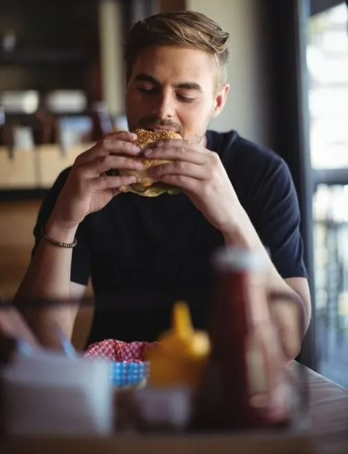 Man Eating a Hamburger at a Table — Pigglys Supermarket, Takeaway & Bottle Shop in The Gap, NT