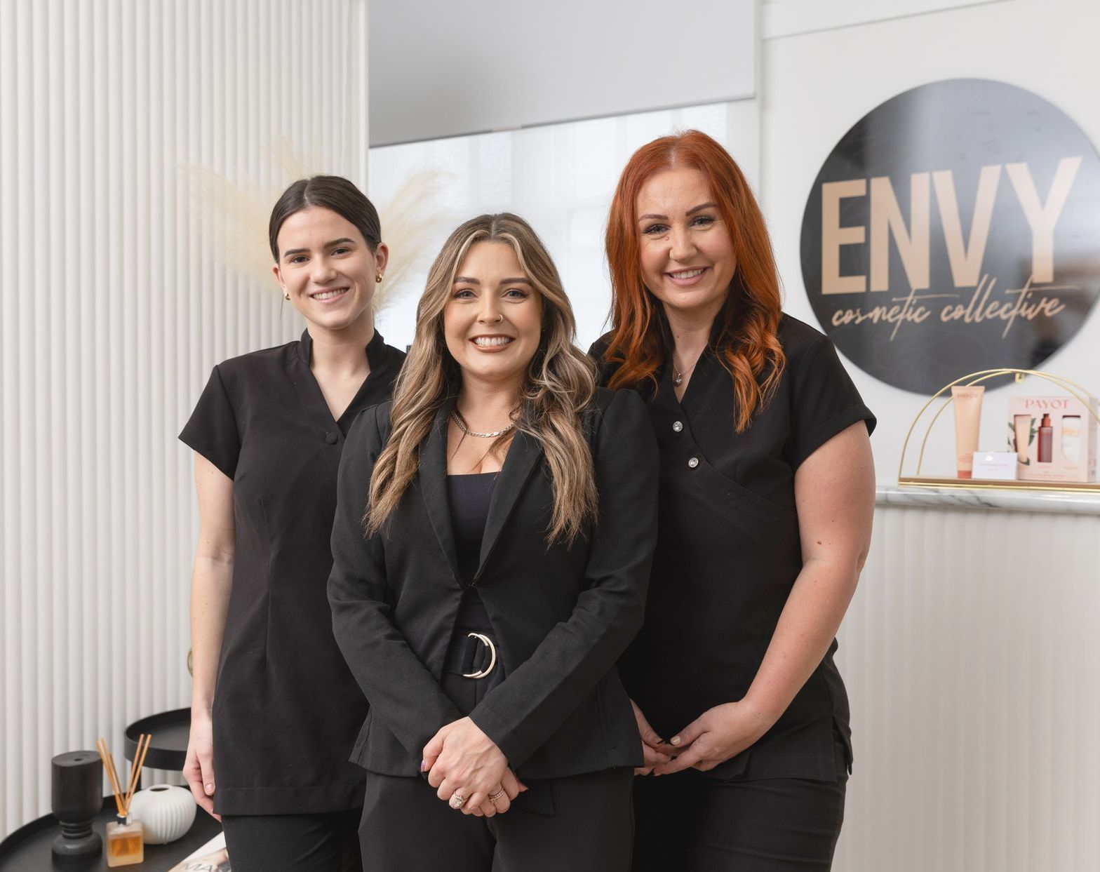 Three Woman Standing At A Counter In Front Of A Sign — Envy Cosmetic Collective in Maitland, NSW