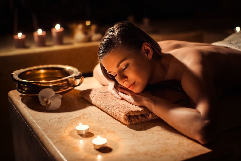A Woman is Laying on a Table With Candles in a Spa — Envy Cosmetic Collective in Maitland, NSW