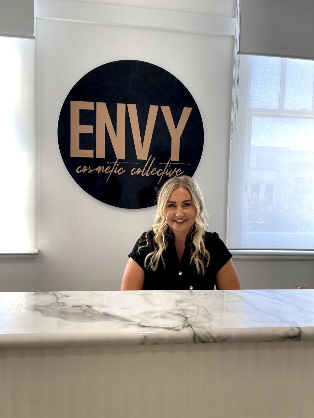 A Woman is Sitting at a Counter in Front of a Sign That Says Envy on It — Envy Cosmetic Collective in Maitland, NSW