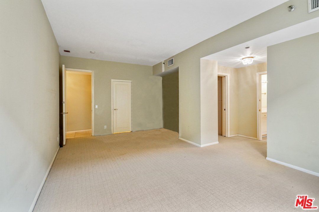 An empty living room with a carpeted floor and beige walls.