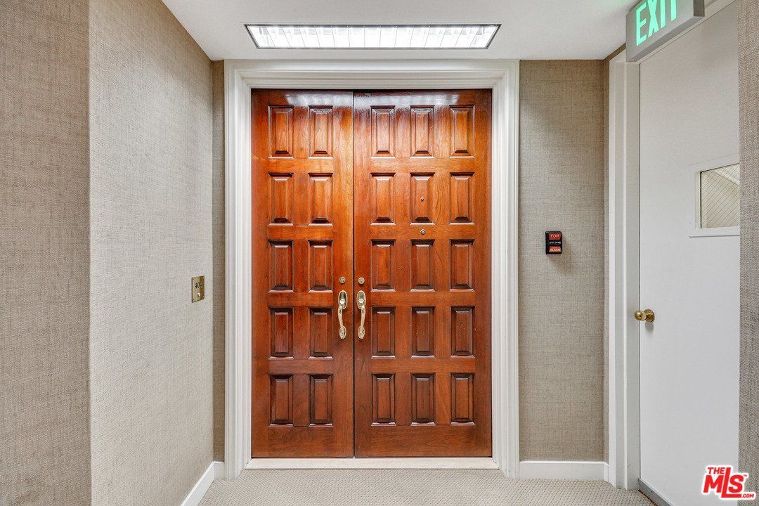 A hallway with a large wooden door and a green exit sign