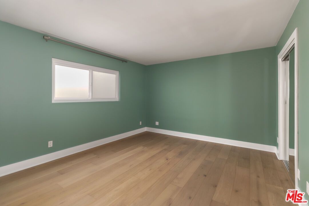 An empty room with green walls and hardwood floors.