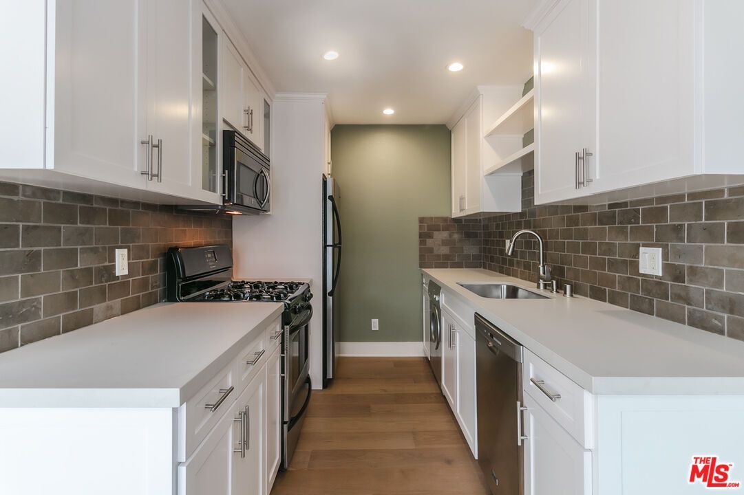 A kitchen with white cabinets , a stove , a refrigerator , and a sink.