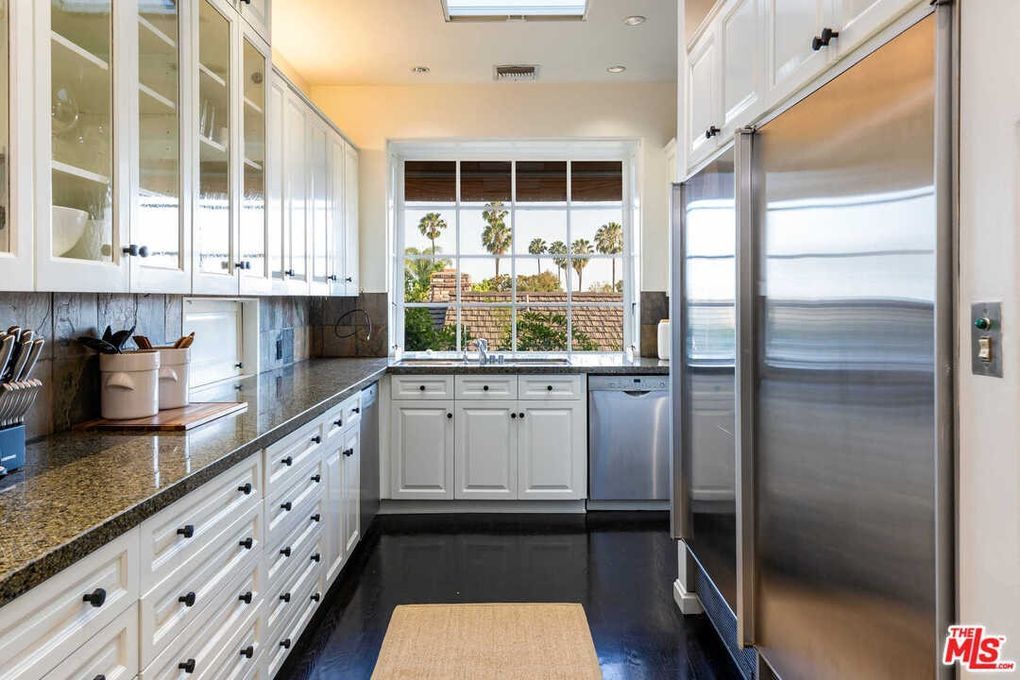 A kitchen with white cabinets and stainless steel appliances and a large window.