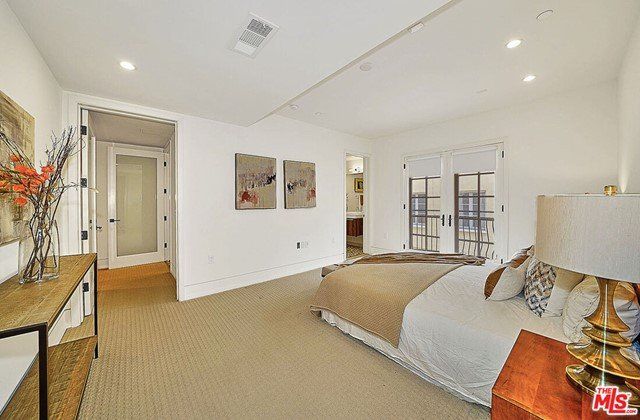 A bedroom with a bed , nightstand , lamp and paintings on the wall.