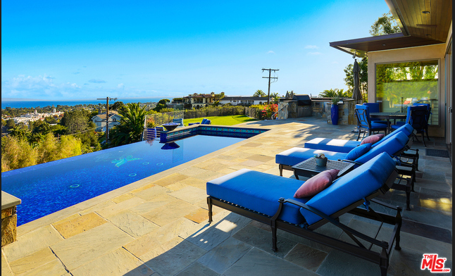 A swimming pool with blue chairs and a view of the ocean