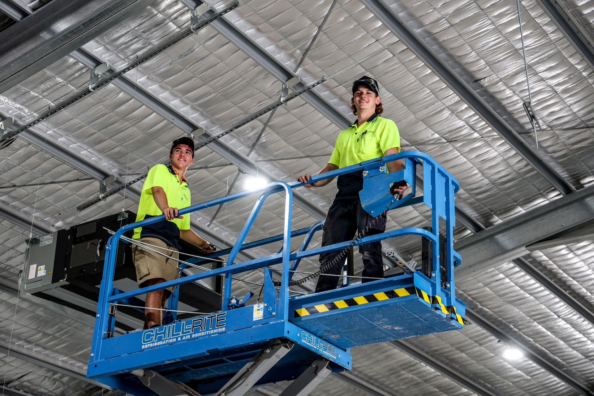 Technicians on a scissor lift to do air conditioning in a warehouse — Chill-Rite Refrigeration and Air Conditioning in Dubbo, NSW