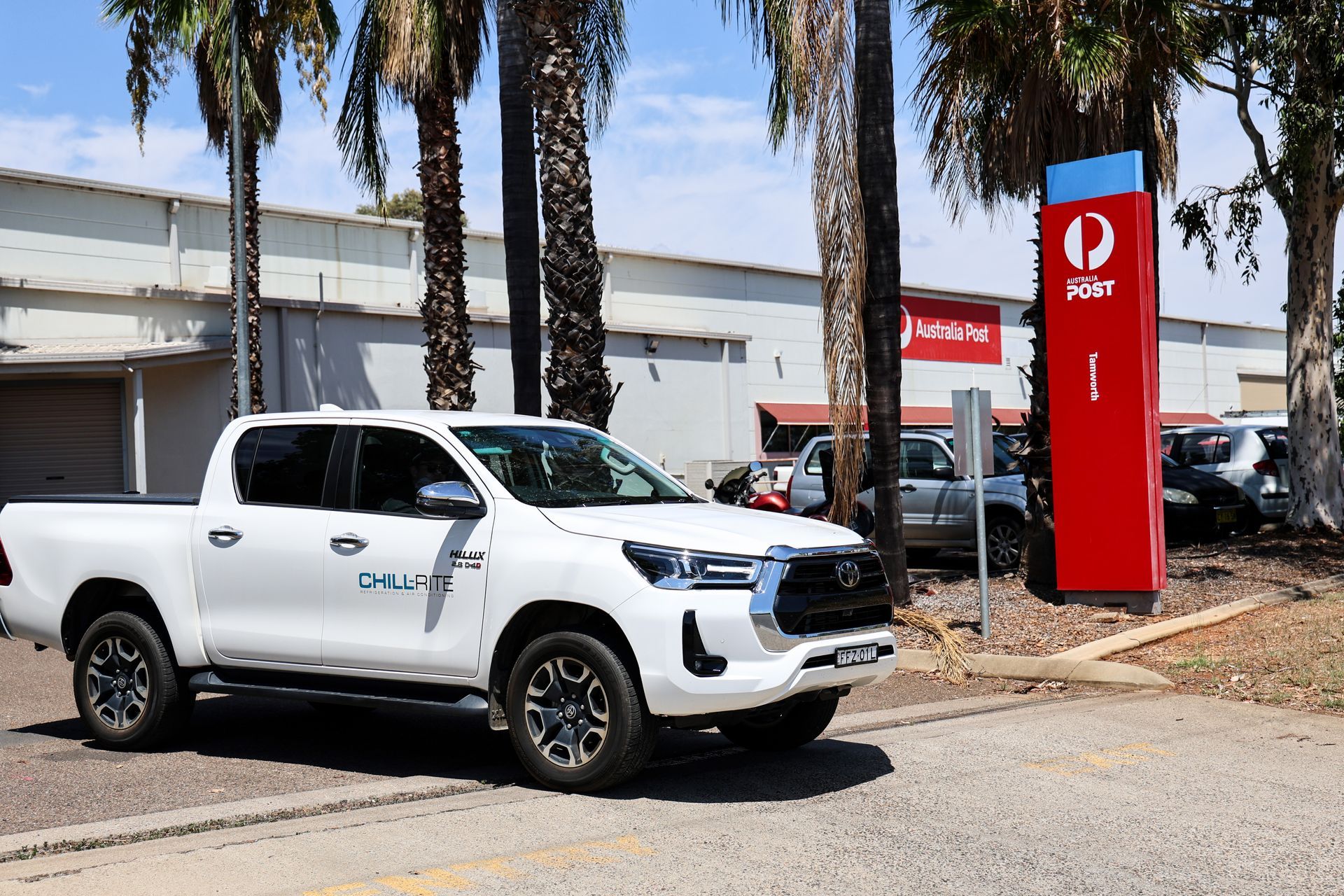 White pickup truck in front of a red Australia Post sign and building, outdoors