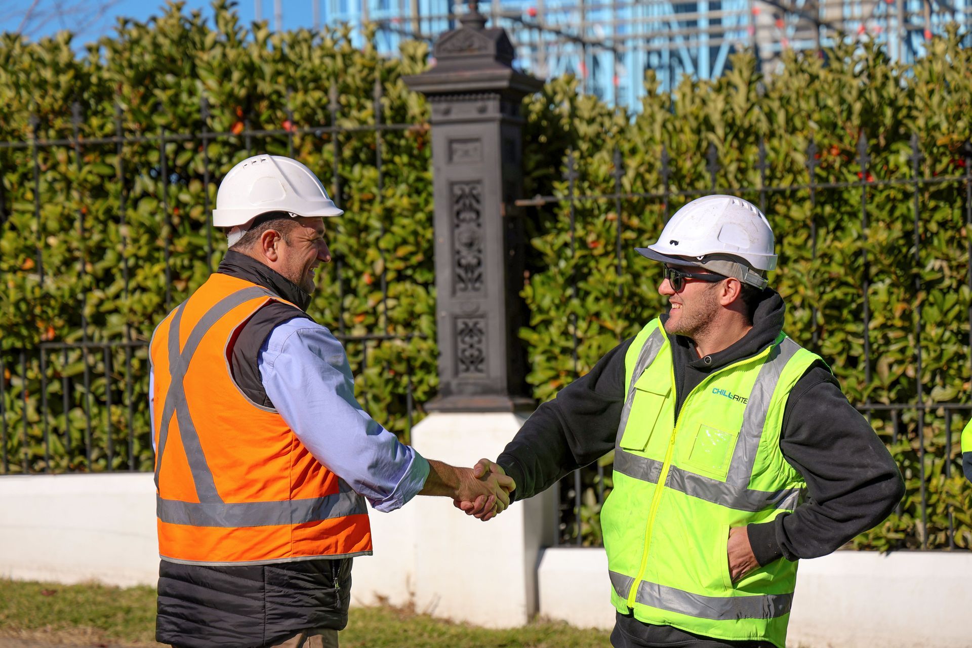 Two construction workers in safety vests and helmets shaking hands outdoors— Chill-Rite Refrigeration and Air Conditioning in Mudgee, NSW