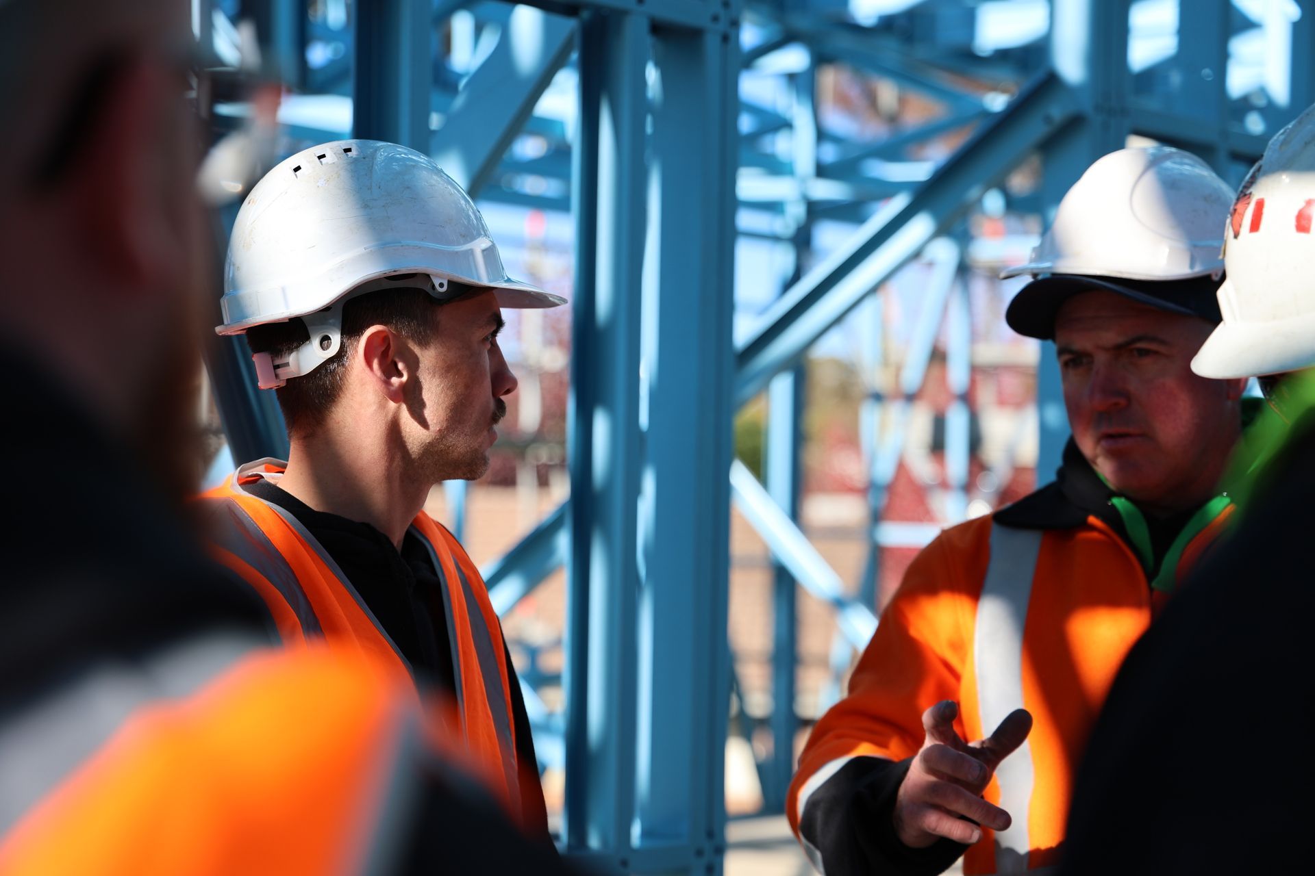 Construction workers in hard hats and safety vests discussing near a blue metal frame— Chill-Rite Refrigeration and Air Conditioning in Bathurst, NSW