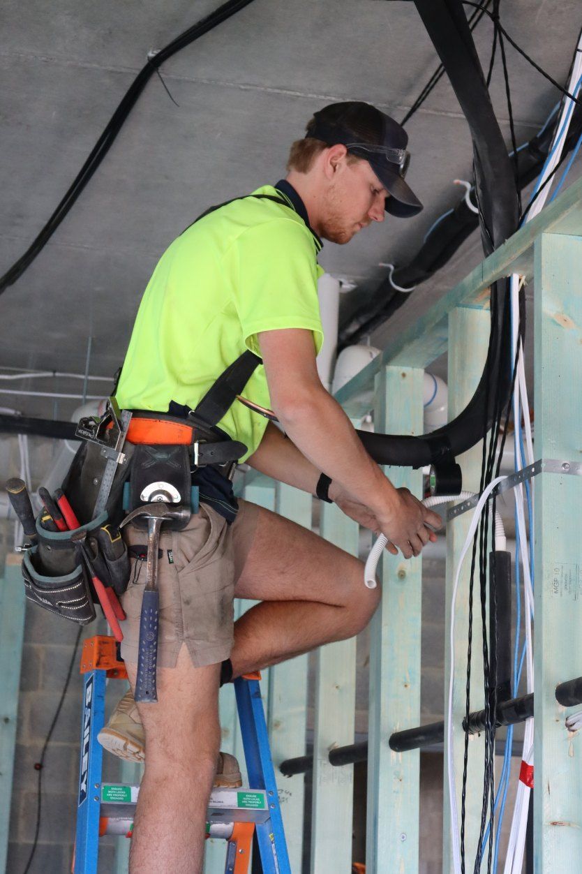 A Man is Standing on a Ladder Working on Wires — Chill-Rite Refrigeration and Air Conditioning in Dubbo, NSW