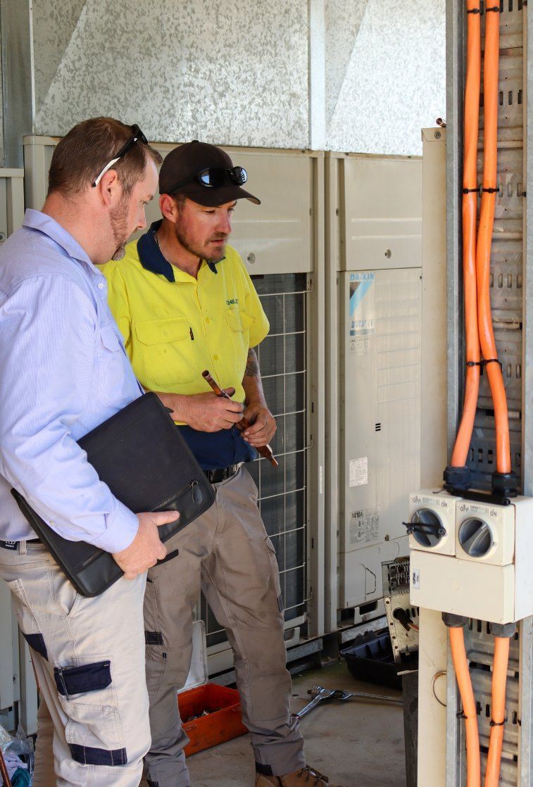 Two Men Are Standing Next to Each Other Looking at a Machine — Chill-Rite Refrigeration and Air Conditioning in Dubbo, NSW