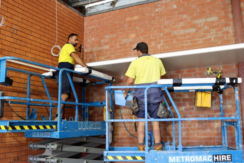 Two Men Are Working on a Scissor Lift in a Brick Building — Chill-Rite Refrigeration and Air Conditioning in Dubbo, NSW
