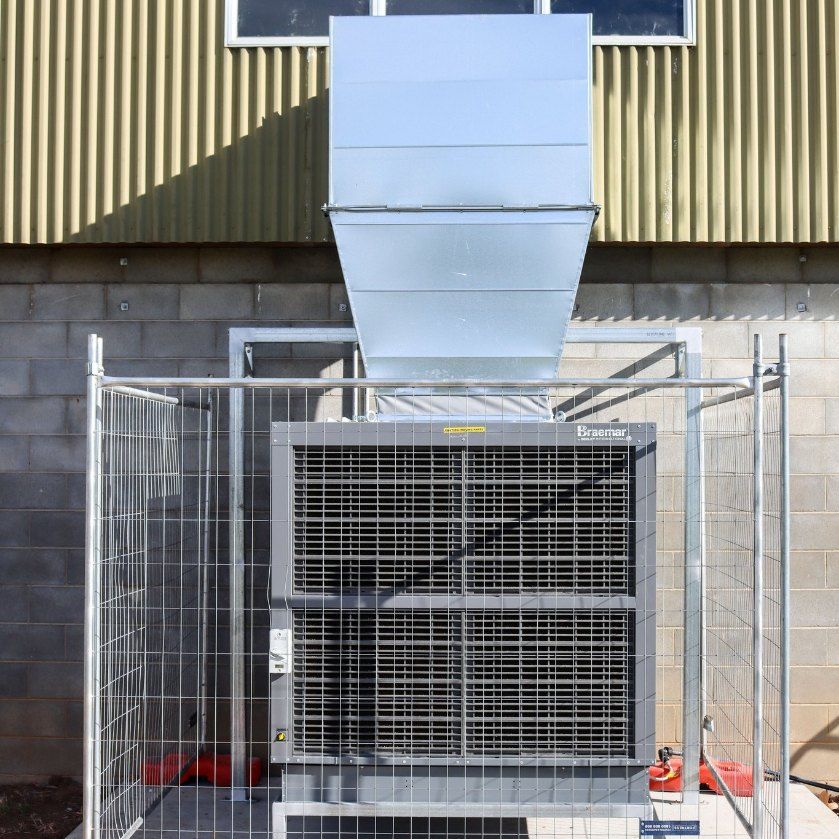 A Large Air Conditioner is Behind a Fence in Front of a Building — Chill-Rite Refrigeration and Air Conditioning in Dubbo, NSW
