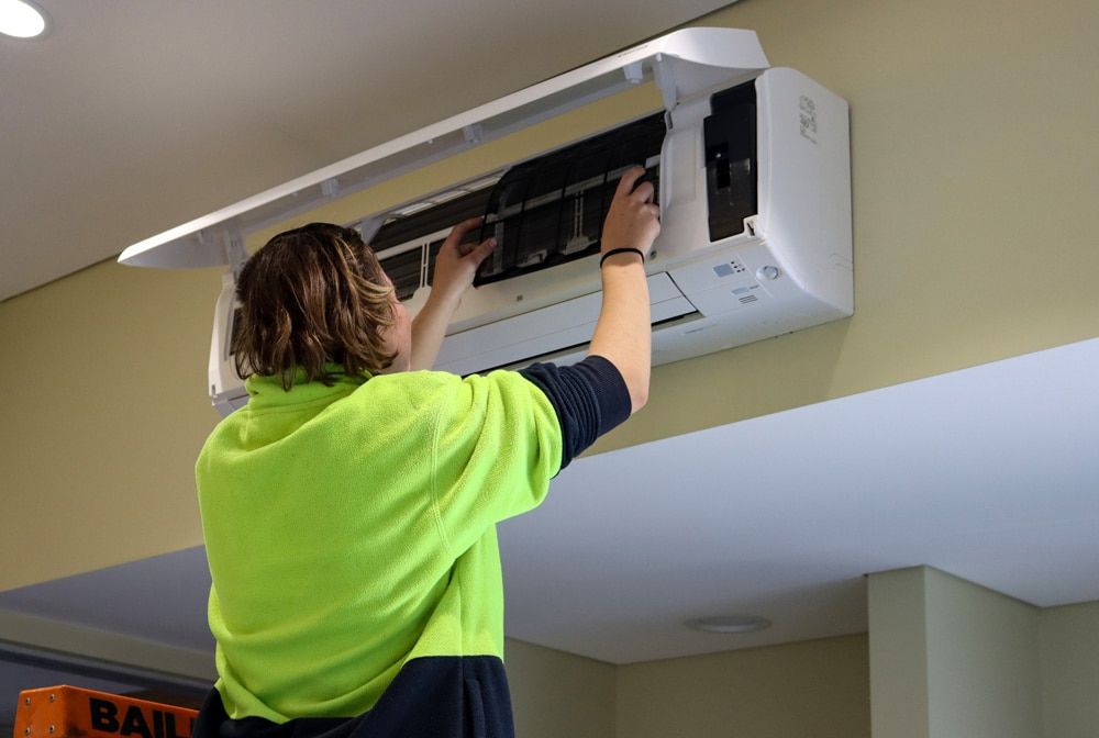 A Woman is Cleaning an Air Conditioner on the Wall — Chill-Rite Refrigeration and Air Conditioning in Dubbo, NSW