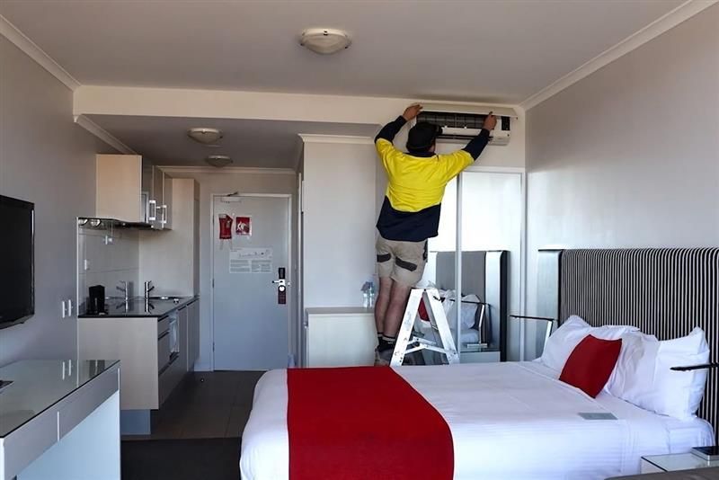Person in yellow shirt installing air conditioner in hotel room— Chill-Rite Refrigeration and Air Conditioning in Newcastle, NSW