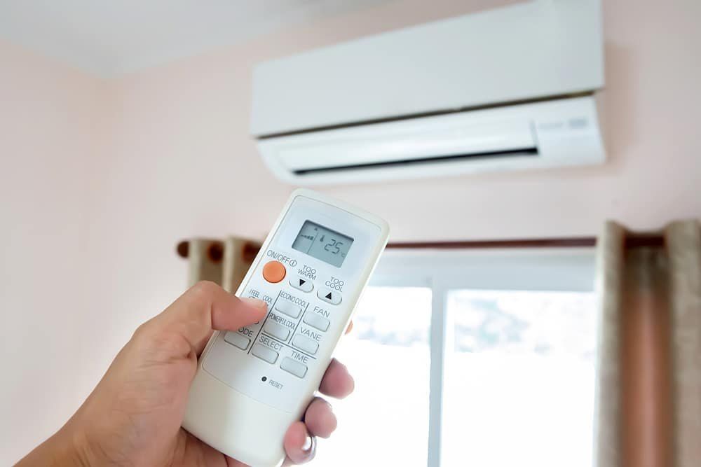 A Person is Holding a Remote Control in Front of an Air Conditioner — Chill-Rite Refrigeration and Air Conditioning in Newcastle, NSW