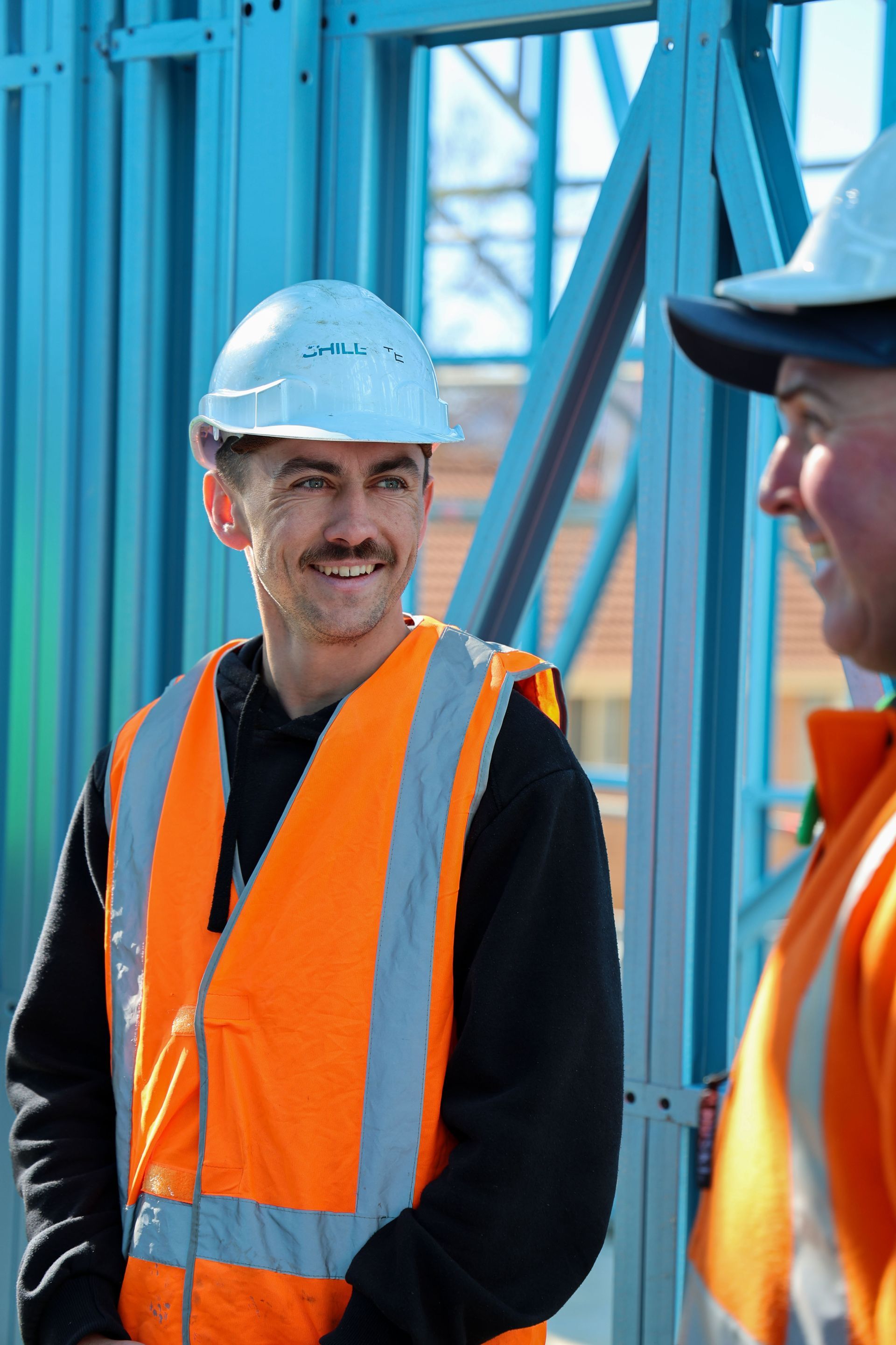 Two construction workers wearing hard hats and safety vests smile at each other, on a construction site— Chill-Rite Refrigeration and Air Conditioning in Dubbo, NSW