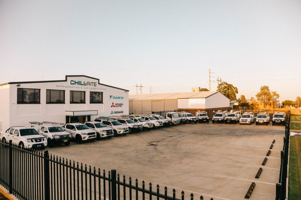 Cars parked in front of a white building with signage. Metal fence in foreground. Sunny day— Chill-Rite Refrigeration and Air Conditioning in Coffs Harbour, NSW