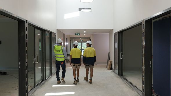 Three construction workers walking down a hallway with glass-panelled doorways; white hard hats and workwear— Chill-Rite Refrigeration and Air Conditioning in Dubbo, NSW