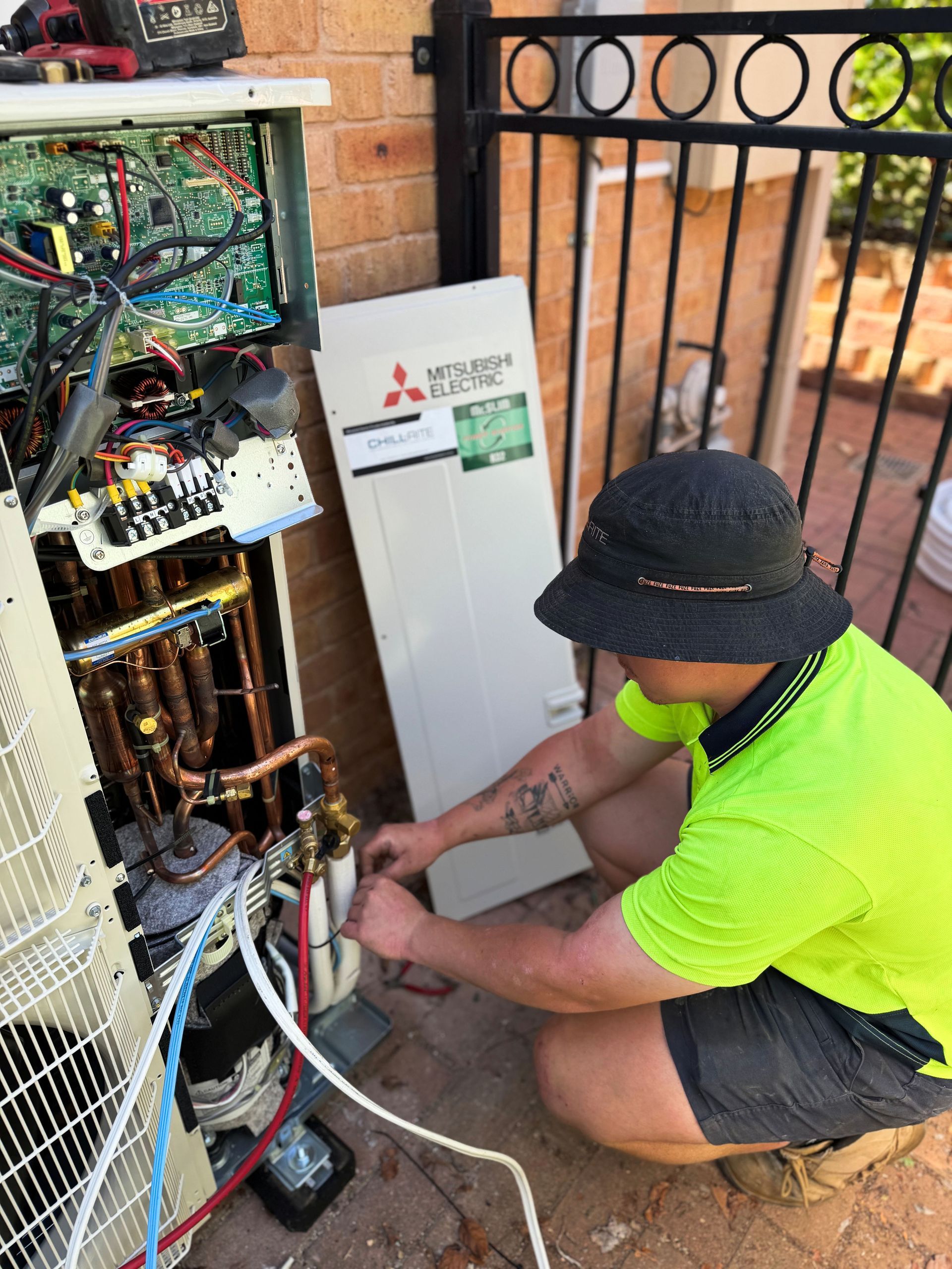 A technician repairing an air conditioning unit outside near a fence— Chill-Rite Refrigeration and Air Conditioning in Newcastle, NSW
