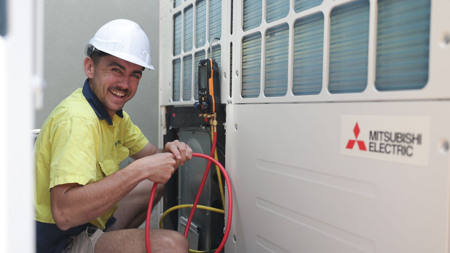 Man in hard hat working on a Mitsubishi Electric air conditioning unit, smiling— Chill-Rite Refrigeration and Air Conditioning in Dubbo, NSW