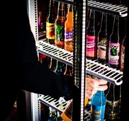 A Person is Reaching Into a Refrigerator Filled With Bottles of Soda — Chill-Rite Refrigeration and Air Conditioning in Dubbo, NSW