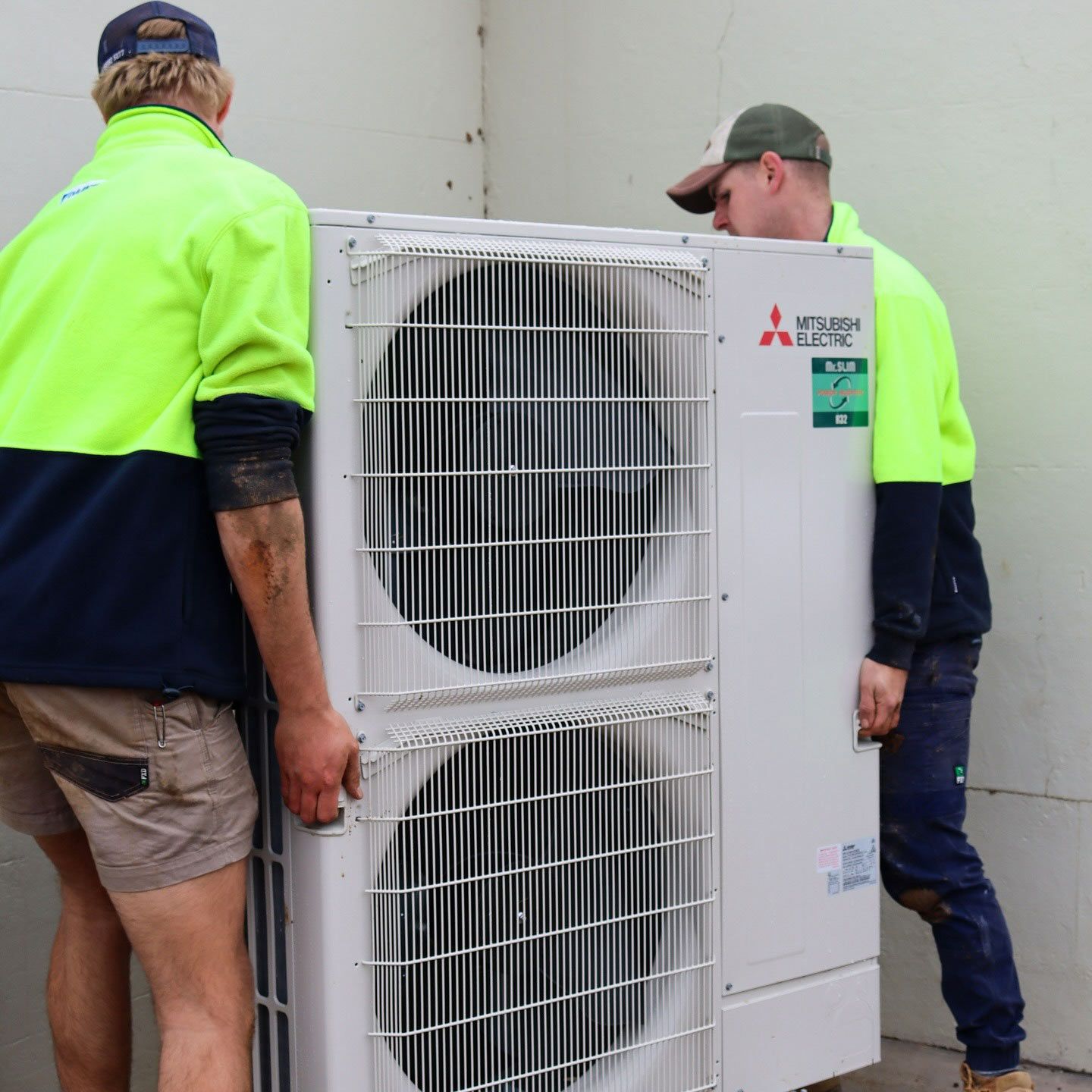 Two Men Are Carrying a Mitsubishi Air Conditioner — Chill-Rite Refrigeration and Air Conditioning in Dubbo, NSW