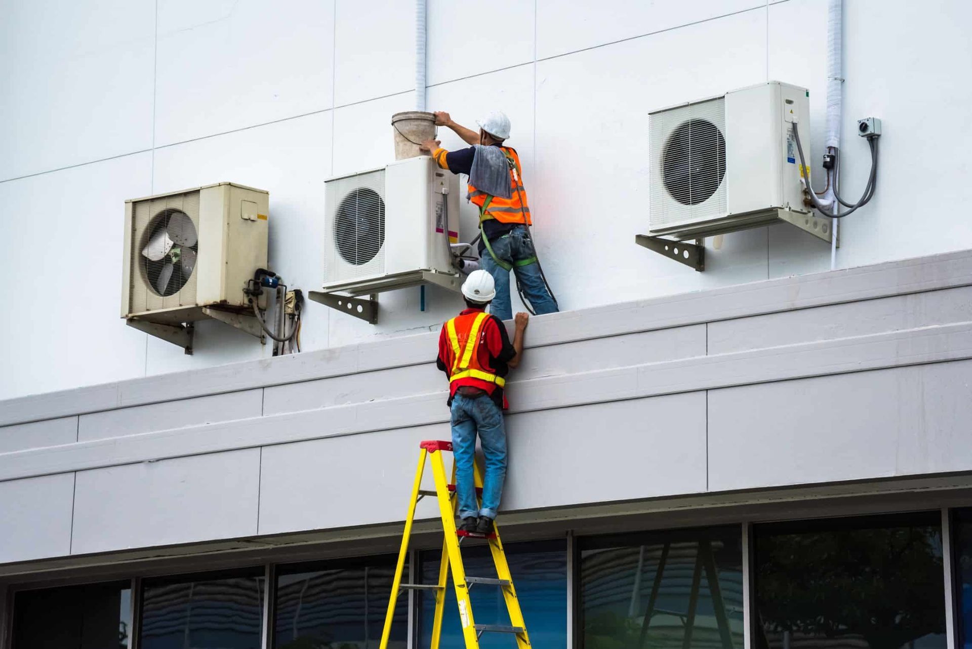 Two Men Are Installing Air Conditioners on the Side of a Building — Chill-Rite Refrigeration and Air Conditioning in Parkes, NSW