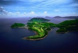 An aerial view of a golf course on a small island in the middle of the ocean.