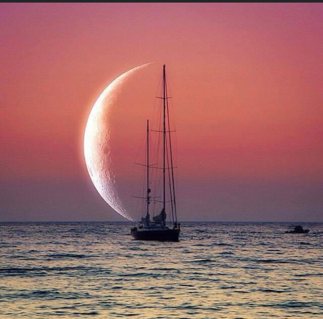 A sailboat in the ocean with a crescent moon in the background