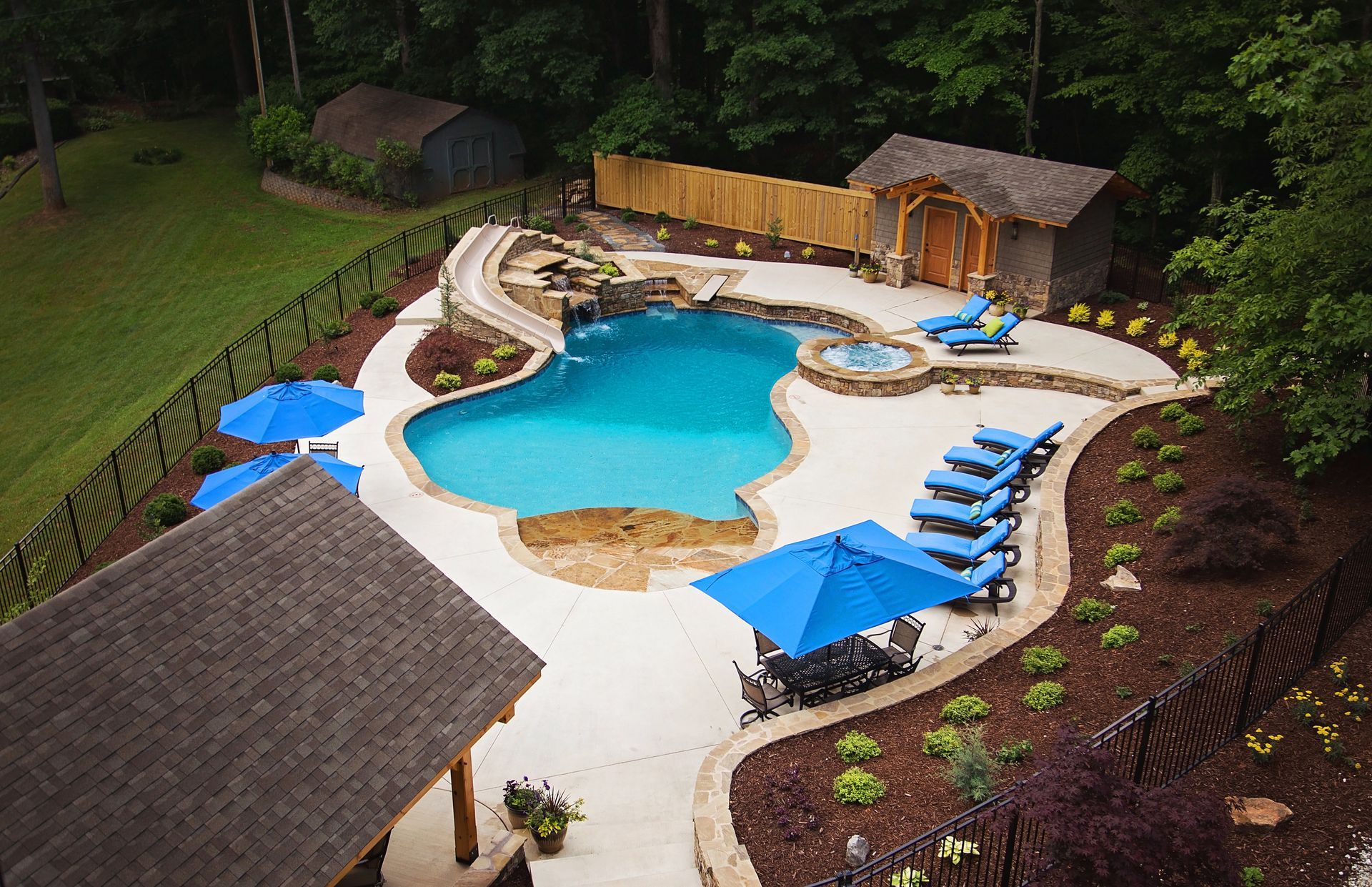 An aerial view of a large swimming pool with blue umbrellas and chairs.