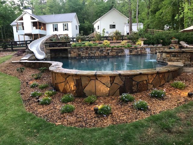 A large swimming pool with a slide in the backyard of a house.