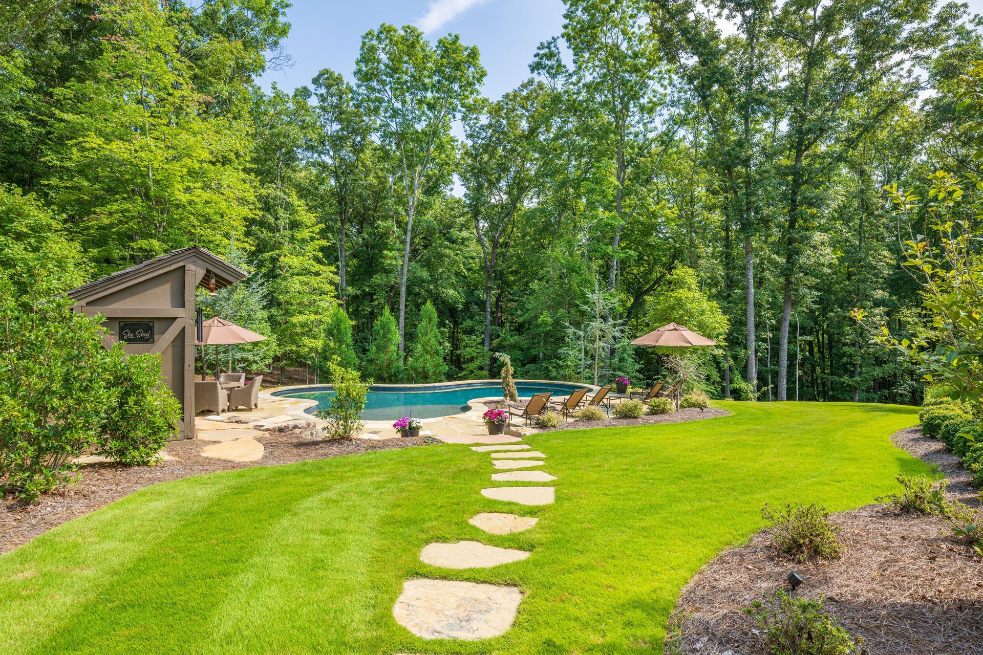 A lush green backyard with a swimming pool and a stone path leading to it.