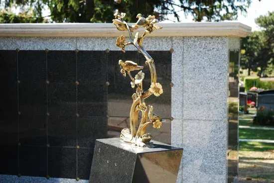 Abstract metal sculpture on a black pedestal in front of a gray stone wall outdoors
